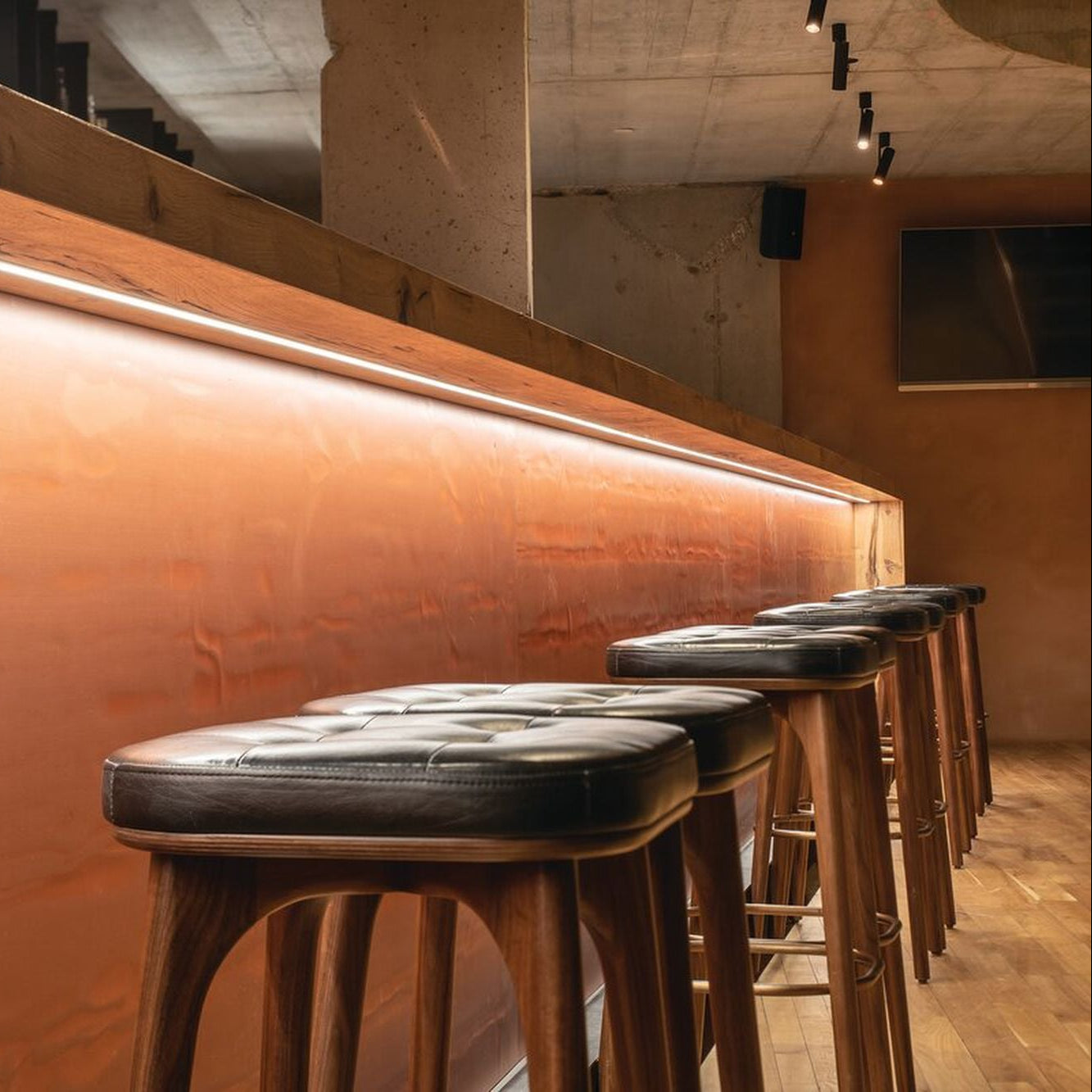 Row of bar stools in front of a wooden bar with warm lighting.